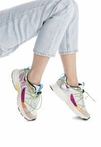 Zapatillas coloridas con acentos metálicos en plata y morado, parte superior de malla, forma redondeada y cordones verdes. Suela de goma ligera.