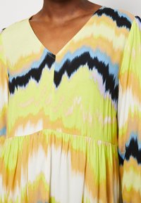 Vestido con escote en V que presenta un vibrante estampado tie-dye en tonos amarillos, verdes, negros y azules; tejido ligero con detalle de cintura plisada.