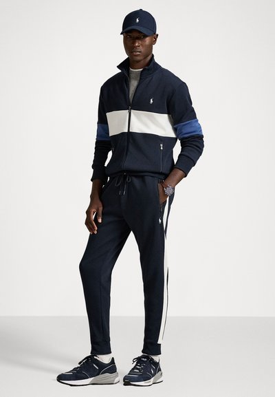 Jūras spēku sporta tērps ar uzvalku, kas satur jaku ar rāvējslēdzēju, kurai ir baltas un zila svītras. Sporta biksēm ir līdzīga krāsu shēma. Baltas sneaker kurpes ar jūras zila akcentiem.