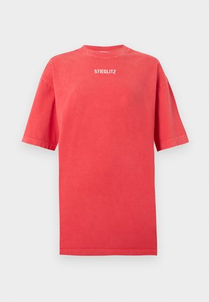T-shirt rouge surdimensionné à manches courtes avec col rond et texte blanc "STIEGLITZ" centré sous le col à l'avant.
