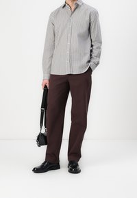 Näppäimistö paidan ykköset ohuilla pystysuorilla raidoilla harmaan ja tummansinisen sävyisessä, paritettu tummanruskeiden housujen kanssa. Mustat kengät ja pieni musta laukku mukana.