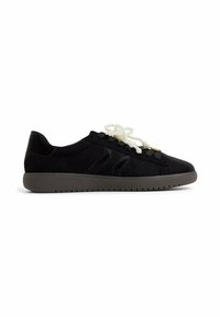Czarne materiałowe sneakersy z teksturowanym wzorem w jodełkę, szara gumowa podeszwa oraz dekoracyjne białe sznurówki przypominające perły.