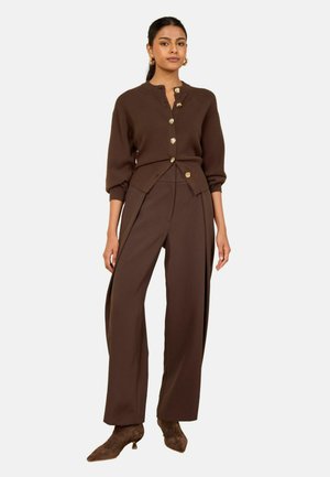 Woman wearing a brown cardigan with gold buttons, matching wide-leg trousers, and brown heeled ankle boots, standing on a white background.