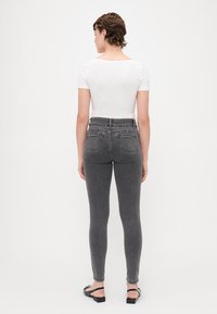 Sive visoko strukirane skinny traperice sa stražnjim džepovima, uparene s prilagođenim bijelim majicama kratkih rukava i crnim sandalama. Glatka tekstura tkanine.