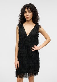 Μαύρο φόρεμα με φούντες, βαθύ V-λαιμόκοψη, αμάνικο σχέδιο και υφή υφάσματος. Διαθέτει στρωμένες φούντες για επιπλέον βάθος και κίνηση.