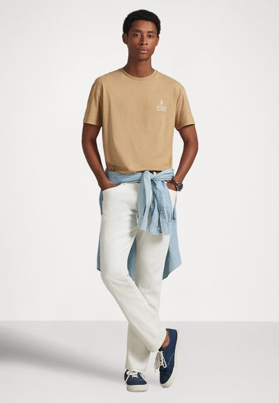 Bēša kokvilnas t-krekls ar izdruku, baltas bikses un zilas džinsa krekls, kas sasiets ap vidukli. Tumši zili apavi ar baltiem zolēm un šņorēm.