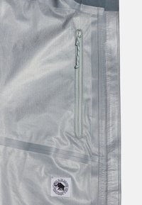 Letvægts sølvfarvet stofpose med en lynlåslomme, struktureret overflade og et logo-patch foran. Søm detaljer langs kanterne.