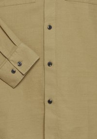 Chemise boutonnée vert olive en tissu texturé, avec des boutons noirs et une poche plaquée sur le côté gauche de la poitrine.