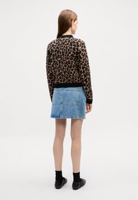 Prindi leopardimustriga jumpers, pruun ja must, on saadud helesinise teksaseelikuga, millel on tagakotid. Mustad kingad ja sokid täiendavad riietust.