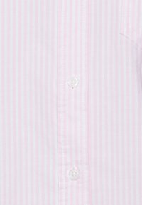 Camicia rosa chiaro con bottoni, caratterizzata da sottili righe bianche, un colletto e una texture di tessuto liscia con un singolo bottone bianco visibile.