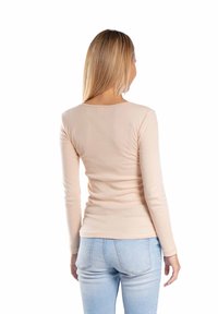 Dopasowana bluzka z długim rękawem w jasnobeżowym, elastycznym materiale, z okrągłym dekoltem i gładką teksturą, połączona z jasnoniebieskimi dżinsami.