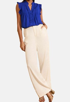 Koningsblauwe blouse met ruches, een knoopsluiting, gecombineerd met crèmekleurige, hooggetailleerde wijde broekspijpen en gouden sandalen met bandjes.