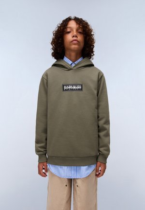 Olive green hoodie with a front logo patch, worn over a blue and white striped shirt. The fabric appears soft and textured.