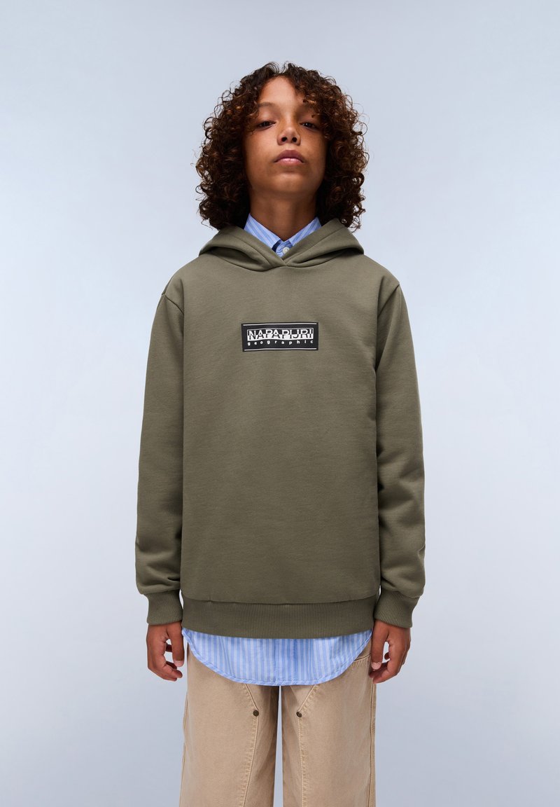 Olivgrüner Hoodie mit einem Logo-Patch auf der Vorderseite, getragen über einem blau-weiß gestreiften Hemd. Der Stoff wirkt weich und strukturiert.