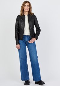 Svart läderjacka, skräddarsydd design, rund halsringning, två framfickor. Kombination med blå utsvängt jeans och svarta ankelstövlar.