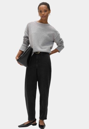 Suéter de punto gris con mangas anchas, cuello alto y puños acanalados, combinado con jeans negros de tiro alto y zapatos planos negros.