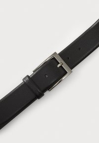 Ceinture en cuir noir avec une finition texturée, boucle en métal argenté portant un logo de marque, et cinq trous ajustables pour un ajustement de taille.
