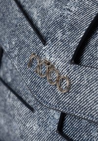 Denim Tasche mit strukturierter Oberfläche, präsentiert in marineblauen und hellblauen Mustern. Silbernes Logo-Element und ein strukturiertes Design mit kantigen Details.