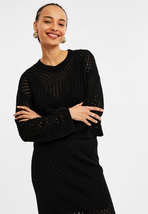 Zwart gebreid sweater met een open structuur, voorzien van een ronde halslijn en geribbelde manchetten, gecombineerd met een bijpassende gestructureerde rok.