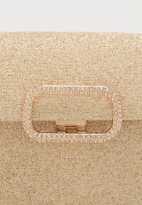 Zlatá kabelka s textúrovaným povrchom, vybavená obdĺžnikovým uzáverom posiatym kryštálmi a kovovým uzáverom.