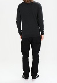 Ciemnoszary sweter z długim rękawem z okrągłym dekoltem, dopasowanymi mankietami i dołem, zestawiony z czarnymi jeansami i czarno-białymi trampkami.