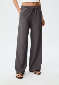 Wide-leg charcoal grey pants made of textured fabric, featuring an elastic waistband with a drawstring and side pockets.