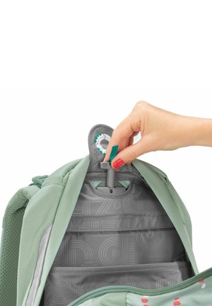 Interno di uno zaino verde chiaro che mostra una fodera grigia a motivo con tasche organizzative. Una mano sta sistemando un componente hardware grigio.