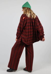 Chemise oversize à motifs rouges avec un pantalon large assorti, présentant des designs géométriques et un bonnet vert. Le tissu semble texturé.