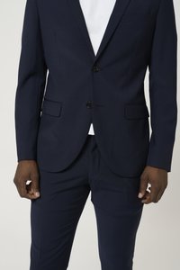 Costume bleu marine avec un blazer ajusté et un pantalon sur mesure. Comprend deux boutons, deux poches avant et une texture subtile dans le tissu.