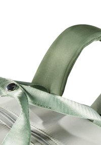 Asa de bolsa de tela verde claro con un acabado suave y una correa texturizada. Acento de botón de metal cerca del área de la cremallera. Diseño compacto.