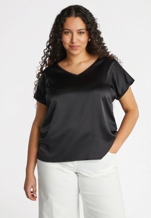 Blusa negra de satén con escote en V y mangas cortas, textura suave, corte relajado, combinada con pantalones blancos, que muestra un diseño simple y elegante.