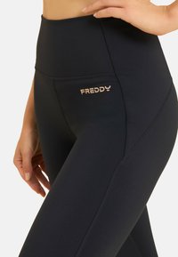 Leggings neri a vita alta realizzati in materiale elasticizzato, con un piccolo logo "FREDDY" in rosa oro sul lato e cuciture piatte per il massimo comfort.