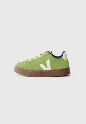 Green suede sneaker with cream accents, featuring laces, a brown rubber sole, and a prominent side logo. Rounded toe and padded collar.