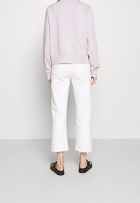 Světlofialová mikina s kulatým lemem, doplněná bílými zkrácenými džínami s třepenými okraji. Černé sandály dokončují outfit.