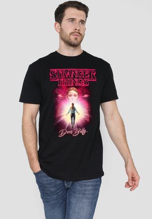 Black cotton t-shirt featuring "Stranger Things" graphic in pink, depicting a character surrounded by elements of light and shadow.