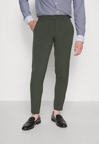 Olivgröna skräddarsydda byxor med smal passform, bälteshällor och knäppning. Kombineras med svarta loafers och en blårandig skjorta.