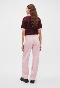 Vīnsarkans apgriezts džemperis ar rozā aprocēm, kombinēts ar gaiši rozā plaša piegriezuma džinsiem un melnām platformas kurpēm, redzams no aizmugures.