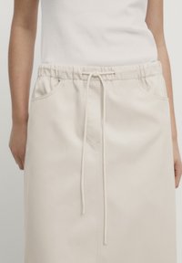 Beige nederdel med elastisk talje og snøre. Har forlommer og et glat, struktureret stof.
