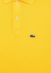 Geel poloshirt van gestructureerde stof, met een twee-knopenbies en een klein groen krokodillenlogo.