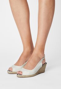 Sandalias cuña de color gris claro con puntera abierta y diseño de tira trasera. El material es un tejido texturizado con una suela de yute trenzado y un acento en el tacón con un patrón.