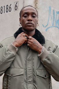 Grøn bomberjakke med sort faux fur krave, ribbede manchetter, dobbelte forlommer og detaljerede sølvringar på hænderne.
