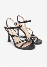 Schwarze High-Heelsandalen mit mehreren gekreuzten Riemen, verziert mit silbernen Pyramidennieten entlang der Kanten und einem schlanken Absatz.