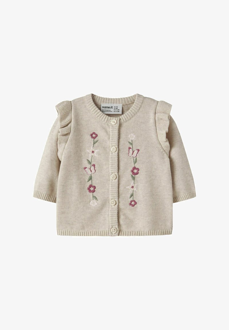 Bež pletena otroška jopica z nagubanimi ramenskimi detajli, zapenjanjem na gumbe ter vezenimi rožicami in metulji v roza in beli barvi na sprednji strani.