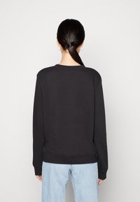 Felpa nera con un classico colletto tondo, maniche lunghe e polsini a costine. Tessuto morbido e vestibilità rilassata, abbinata a jeans azzurri chiari.