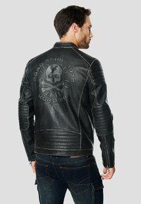 Zwarte leren motorjack met geribbelde details op de schouders en ellebogen; met een afbeelding van een schedel en gekruiste beenderen op de rug.