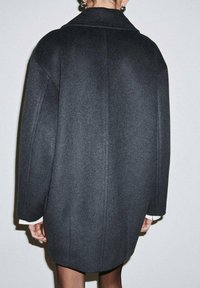 Abrigo de lana gris oscuro de gran tamaño con cuello ancho, corte holgado y detalles visibles de costuras. El abrigo tiene bolsillos laterales y una textura suave.