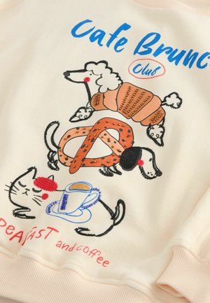Krämfärgad sweatshirt med lekfull broderi av en pudel, croissant, pretzel, tax och katt med en kaffekopp. Texten säger "Café Brunch Klubb."