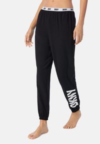 Zwarte joggpants met een witte elastische tailleband met de tekst "DKNY". Met manchet bij de enkels, met "SKNY" in het wit gedrukt aan de zijkant.
