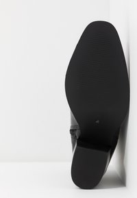Chaussure habillée en cuir noir vue du côté de la semelle, avec un petit talon et une semelle texturée antidérapante.