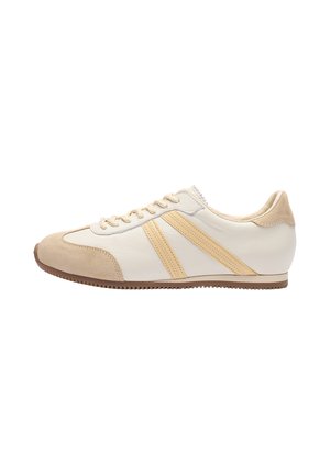 Flacher Sneaker in Beige und Weiß mit Wildleder-Zehenkappe, zwei parallelen gelben Streifen an der Seite, beigen Schnürsenkeln und Gummisohle.